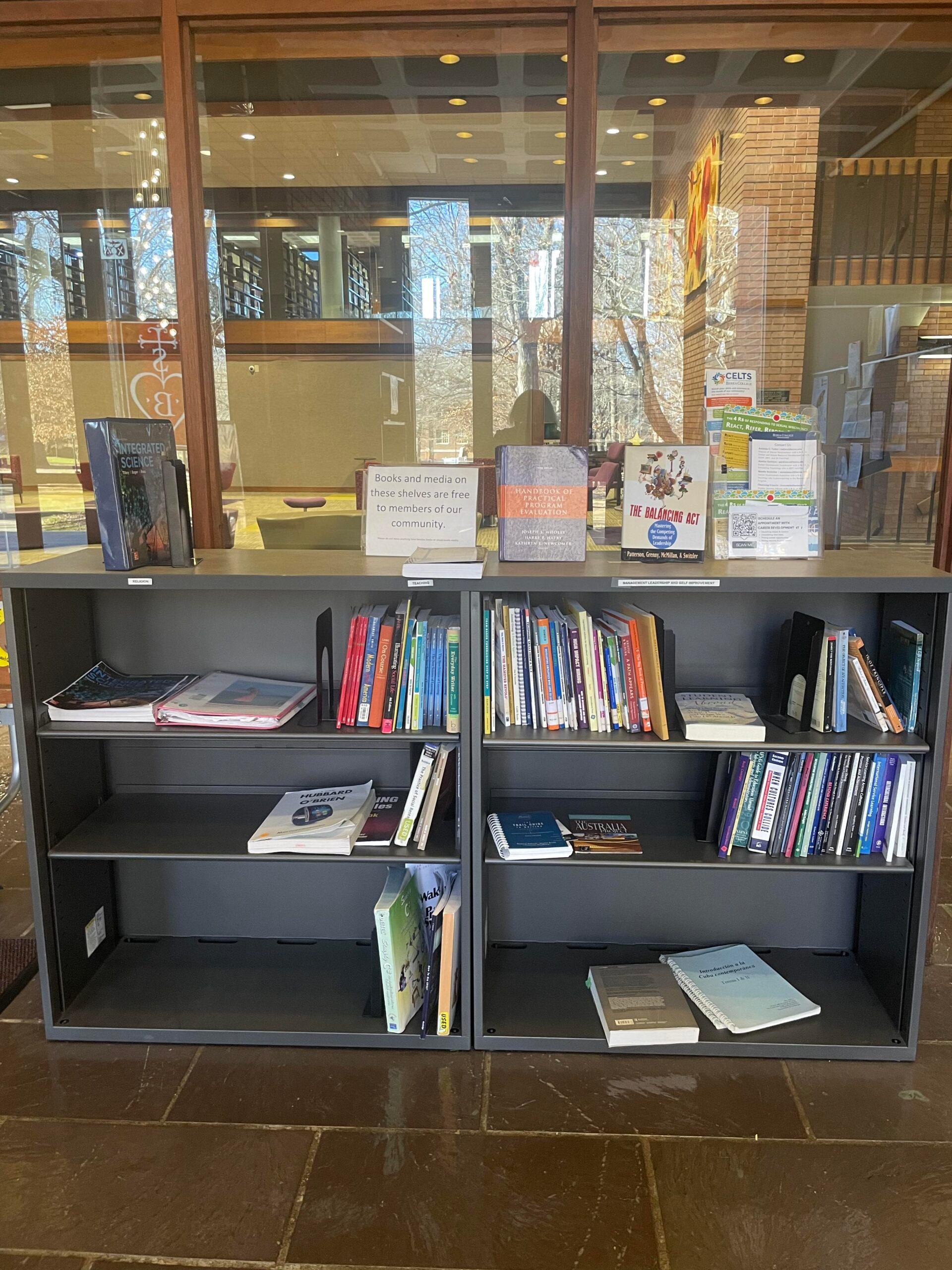Book shelf near windows and entrance of library containing books for students to use for academics or personal use.