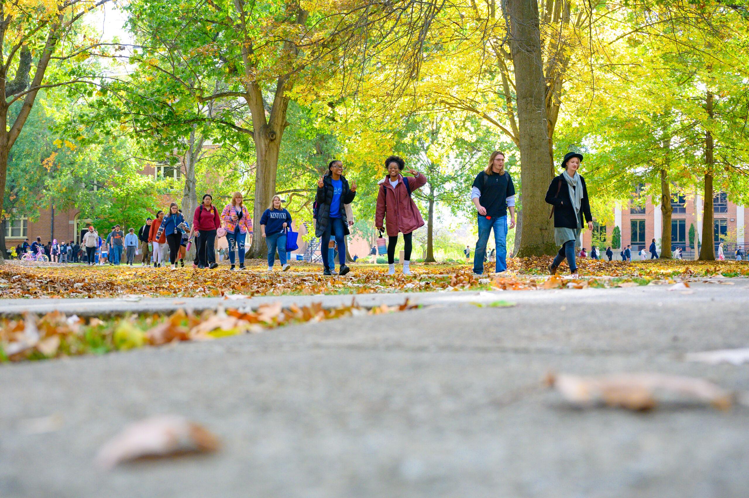 Students in the Quad in the fall, waving and smiling at the camera.