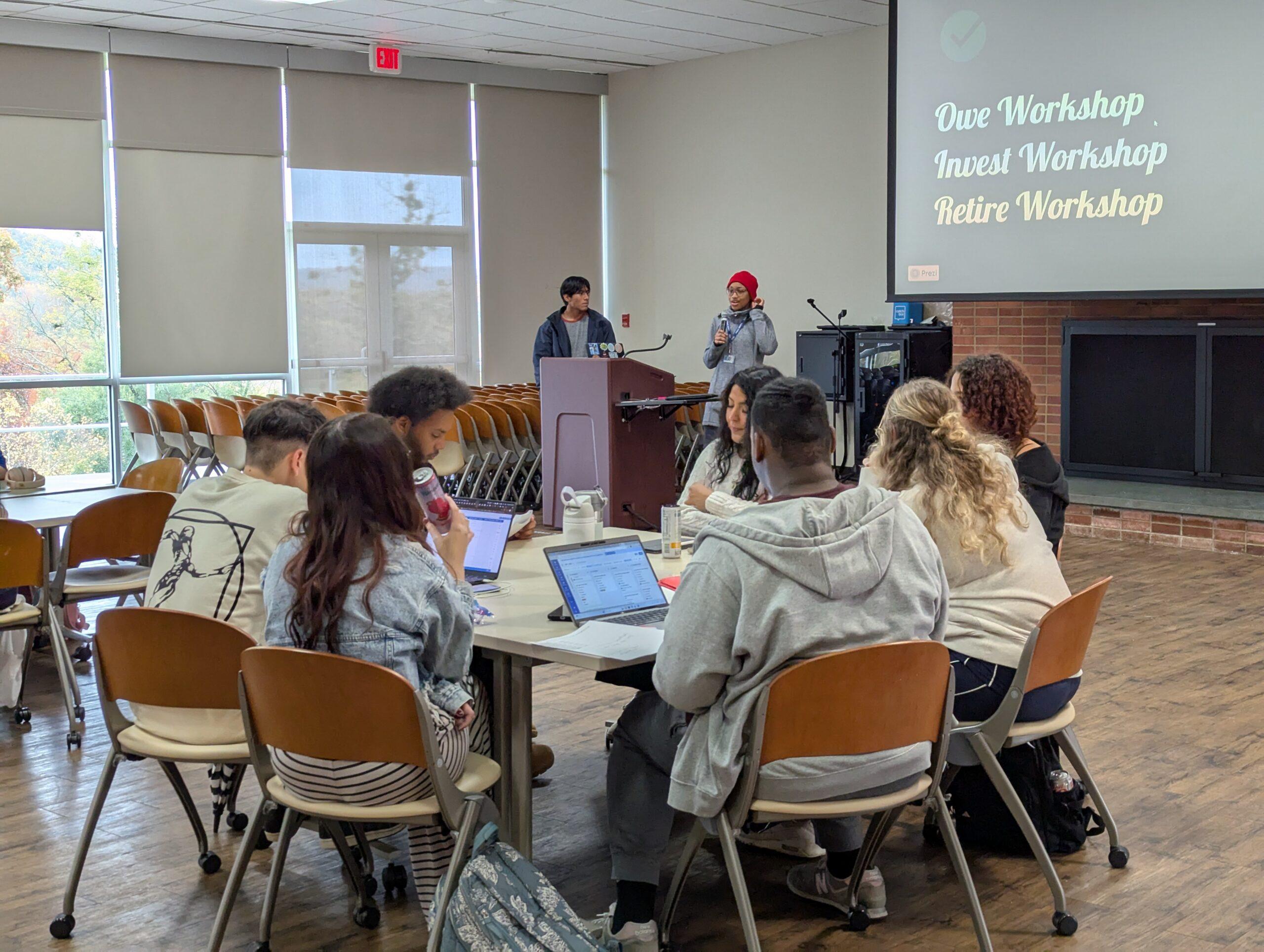 Seven students sit around a rectangular table and listen to an instructor lead a workshop